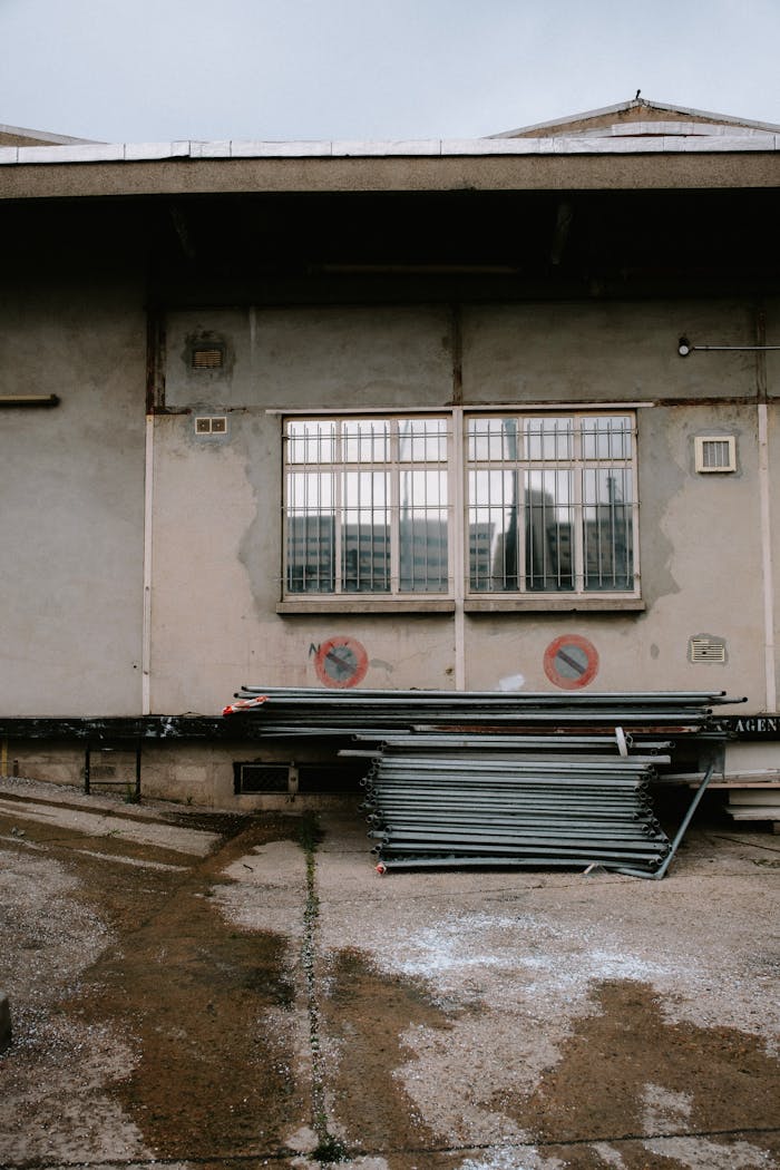 hero-services A weathered warehouse exterior showing stacked metal beams and barred windows.