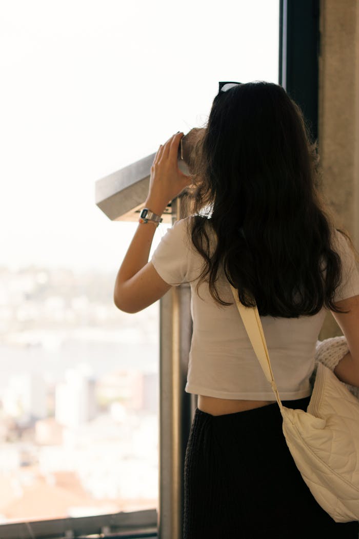 hero-contact A woman in a white shirt explores Istanbul through a telescope, capturing city views.