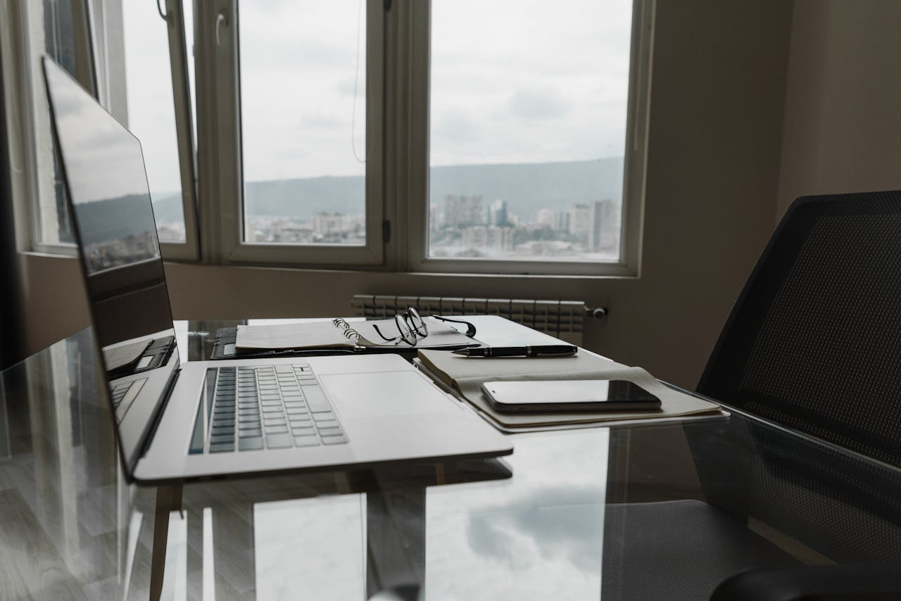 services-04 A sleek office setting with a laptop, notebook, and city skyline view through the window.
