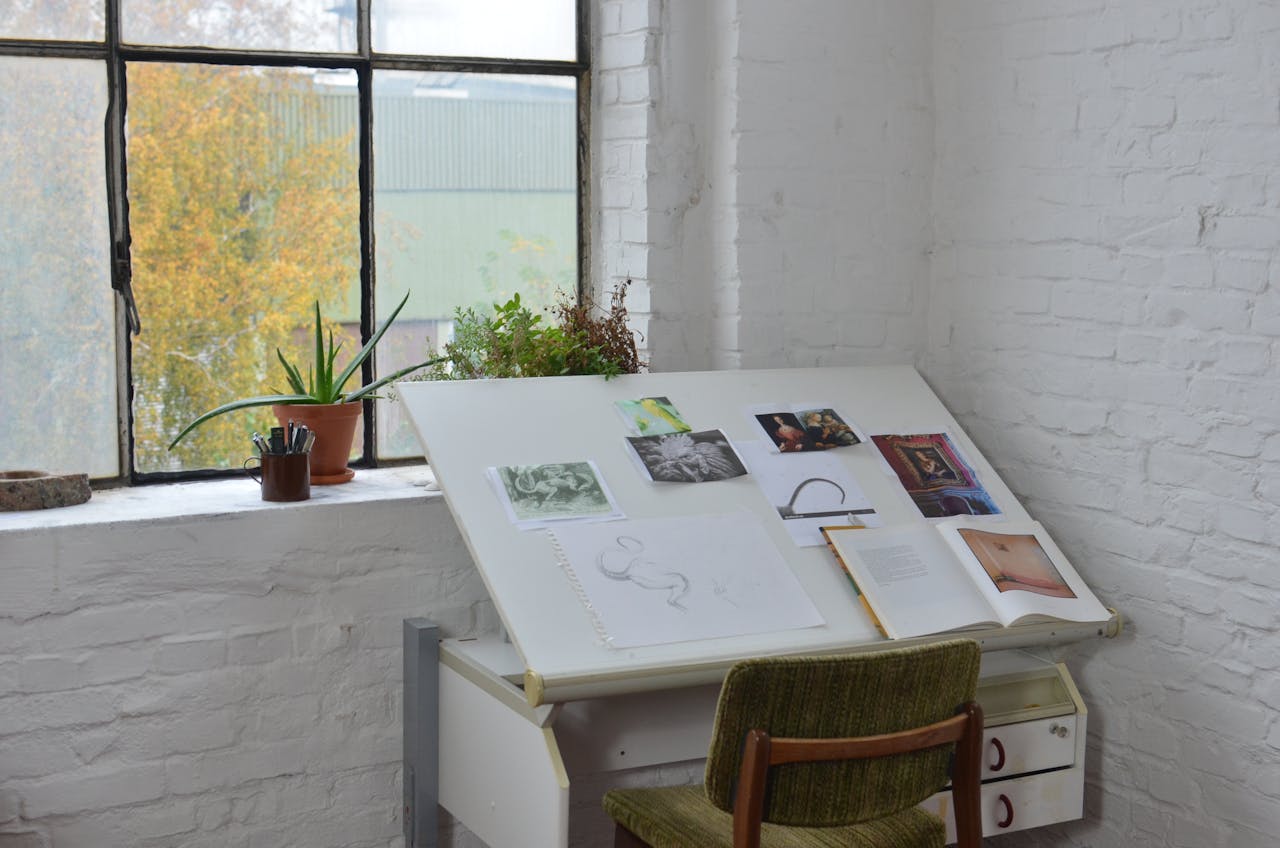 services-03 Opened books with various pictures and sketch placed on drawing table near window in workshop